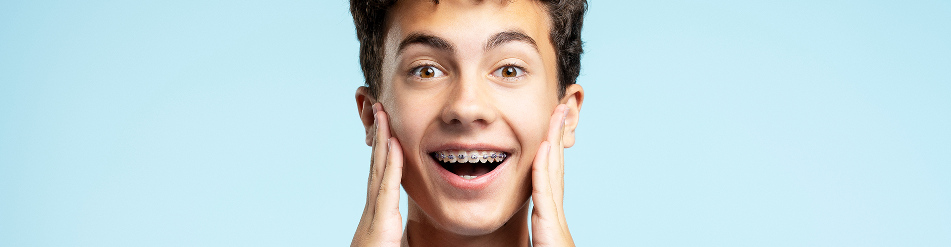 boy with braces holding hands on his cheeks